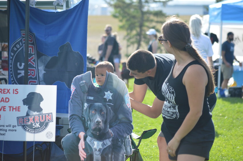 Samantha Urso watches as her husband, Randy Urso, holds up their son, Hudson, 1, behind the cardboard cutout set up at the “RexRun for PAWSitivity” event, held Aug. 6 at Dove Valley Regional Park.
